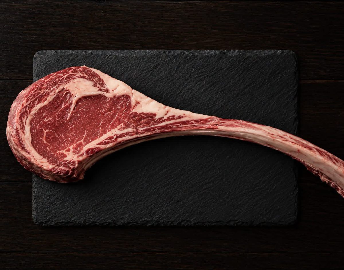 A grass-fed tomahawk ribeye on a black slate board